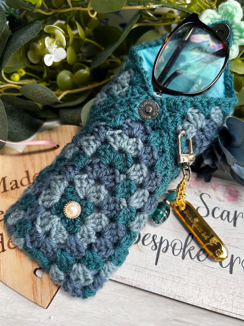 Teal crochet glasses case holding black glasses