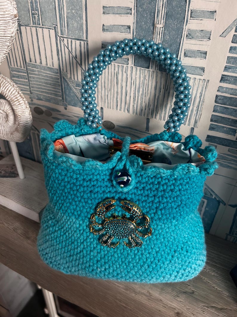 Turquoise crochet handbag with crab embellishment and button closure