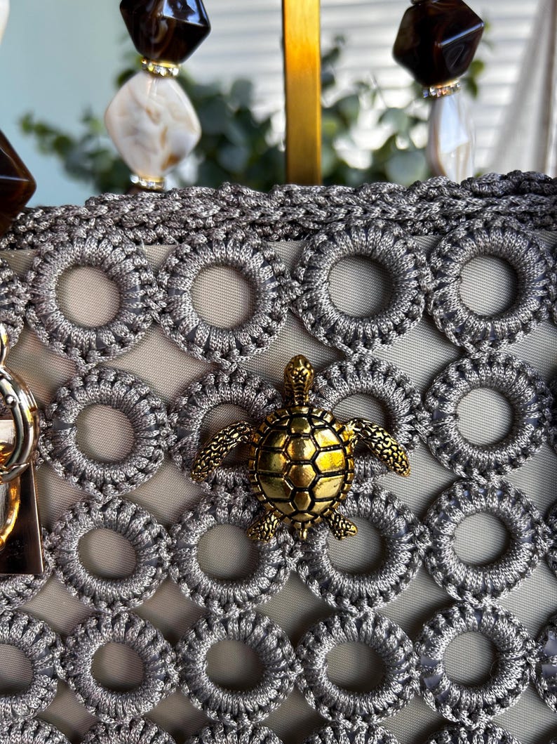 Close-up of gray crochet bag with gold turtle charm and beaded strap