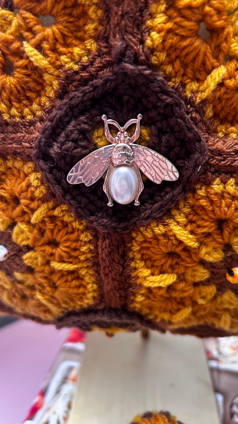 Close-up of crochet tote with rose gold bee and pearl brooch