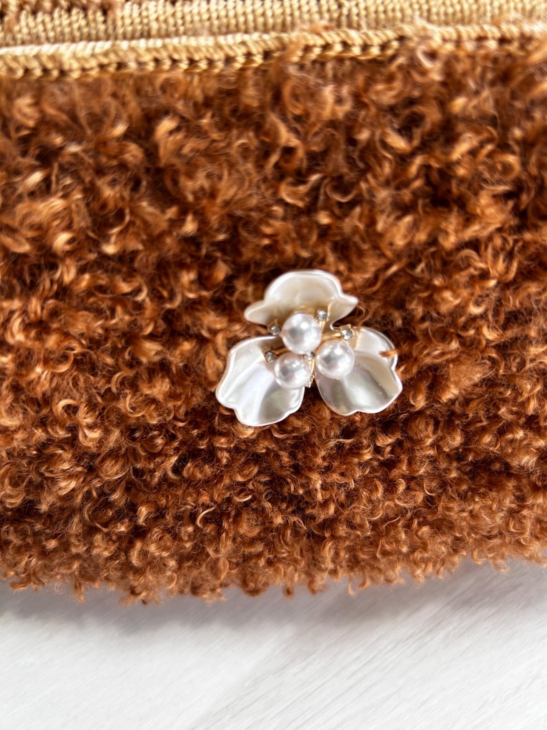 Close-up of white pearl flower brooch on brown bag