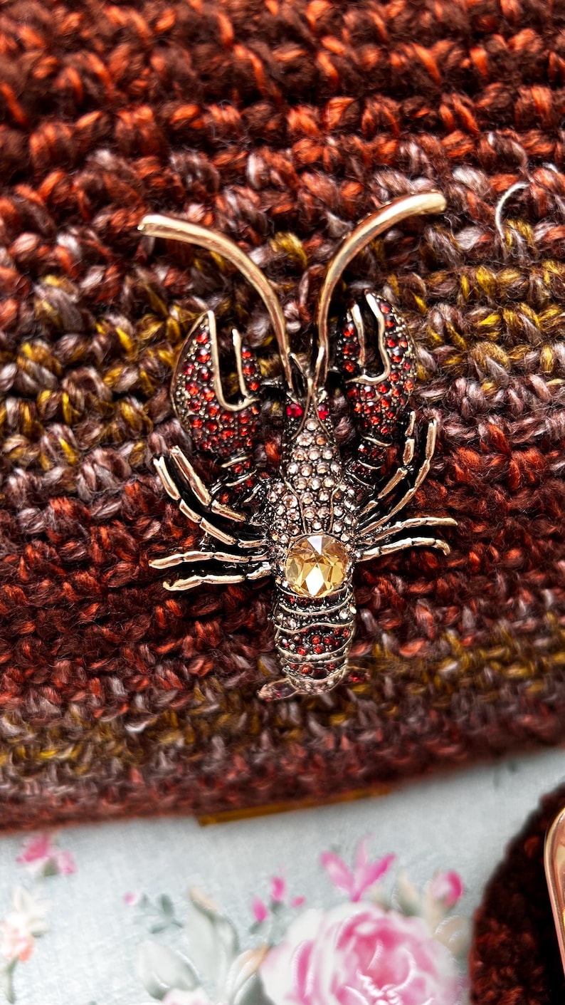Close-up of metallic lobster brooch with crystals on brown crochet